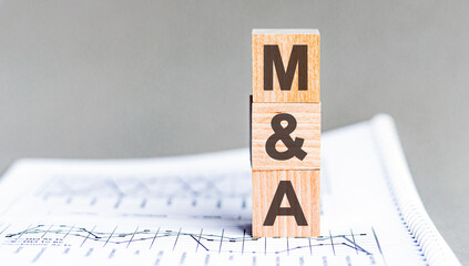 text MA - Mergers and Acquisitions - acronym concept on cubes and diagrams on a gray background,...