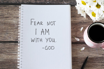 Fear not I am with you, God. Handwritten text in notebook with flowers and cup of coffee on wooden...