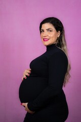 woman with pregnant belly against a purple background wearing a black long sleeved top