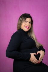Fototapeta premium Smiling pregnant woman making a heart shape with both hands