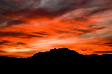 Sunset in red and orange hues over the silhouette of Granite mountain in Prescott, AZ.