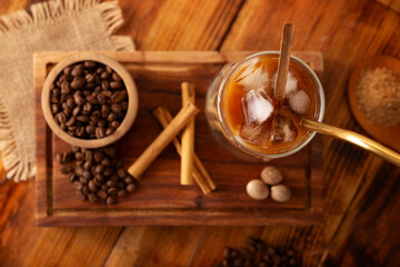 Iced coffee served in a double-walled glass cup and metal straw, a cold summer drink prepared with ice cubes and spices, cinnamon, nutmeg, vanilla, muscovado sugar and cream.