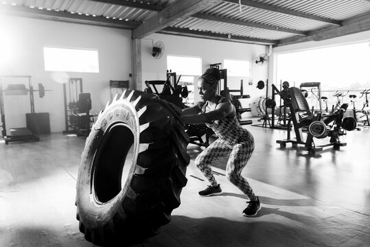 Woman performing tire flipping exercise in gym setting, showing strength and determination