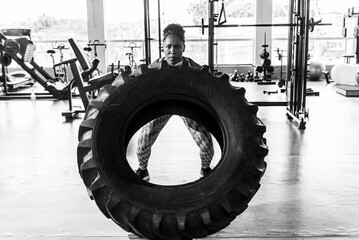 Woman performing tire flipping exercise in gym setting, showing strength and determination