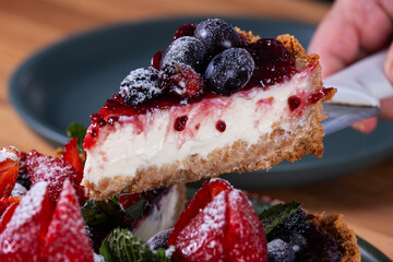 hand holding a slice of sweet pie with cream topping and berries