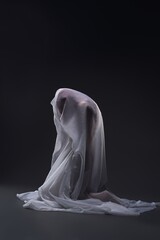 Unrecognizable woman with veil covering body kneeling in studio