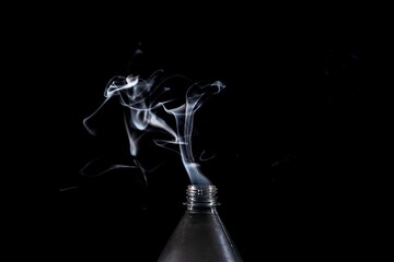 Plastic bottle with its lid off emits a plume of smoke into the air on the dark background