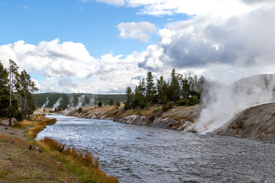 View of Firehole river looking downstream from Firehole bridge, Image shows the hot steaming spring water from the grand prismatic spring running into the river with slightly cloudy skies