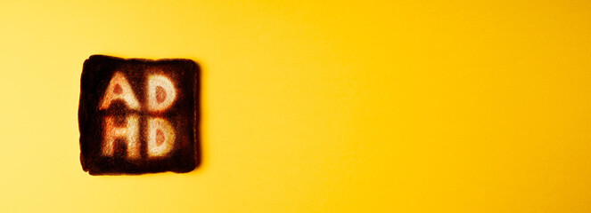 slice of dark burnt charred white bread with word ADHD on it on yellow background. Conceptual image...