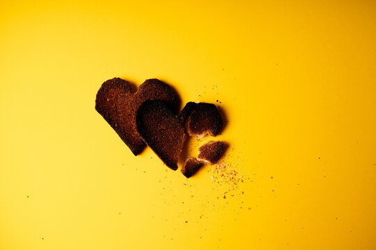 Broken hearted. Two burnt hearts made of white toast bread on yellow background. Conceptual romantic traumatic relationship idea