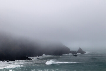 Rocks off route 101 coastal highway during a storm, Image shows the rough Pacific ocean swells hitting the cliffs and low level fog and mist covering the bay 