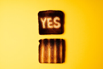 yellow poster with two burnt slices of white bread toast with the word Yes on it.  passionate ardent agreement. creative concept composition - obrazy, fototapety, plakaty