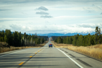 road to the mountains, image shows a endless road heading towards the mountains with a few vehicles on the road and a mountain range in the distant, with grey clouds above, taken october 2023