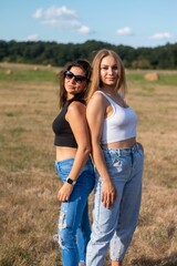 two women in ripped jeans standing on a grassy field, one wearing sunglasses and the
