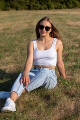 a beautiful woman wearing sunglasses is sitting on the ground and holding her hands behind her