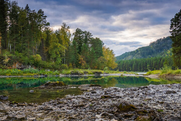 Idyllic view of calm lake and rocky shore with autumn trees in background against cloudy sky at Altai, Russia 