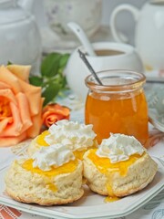 Scones with apricot jam and whipped cream on a table with jar of jam