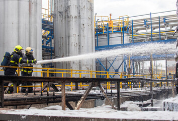 Firefighters with breathing apparatus use foam to extinguish a fire of flammable liquids in a...