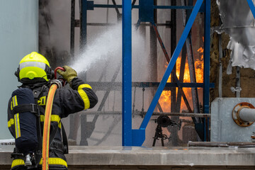 Firefighter with a breathing apparatus uses water to extinguish a fire of flammable liquids in a...
