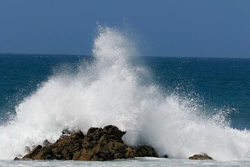 Fototapeta na wymiar Closeup of blue waves crushing on rocks on a sunny day