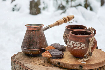 Turk and clay cups with coffee on a wooden stump in a snowy winter forest