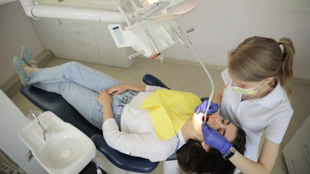Top view of a pleasant nice girl visiting her dentist who is treating her teeth.