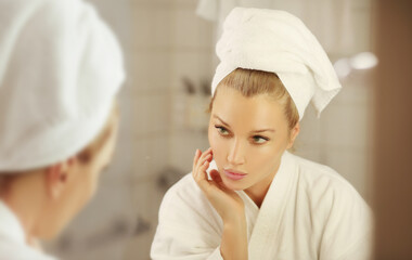 woman looking in the mirror in the bathroom and taking care of her skin.