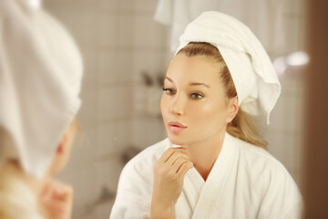woman looking in the mirror in the bathroom and taking care of her skin.
