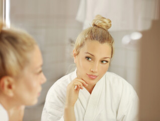 Obraz premium woman looking in the mirror in the bathroom and taking care of her skin.