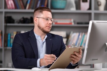 Male psychoanalyst with clipboard working on pc