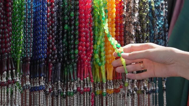 Plastic Rosary Market Overview, Buyer Hand Touching and Choosing Colorful Plastic Close-up on Market. Religious beads with colorful strings. Beautiful muslim rosary nom. Colorful chaplets for prayers.