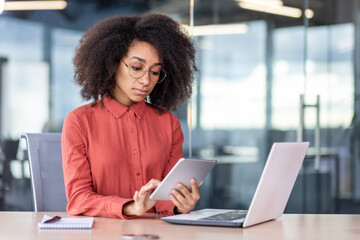 Serious confident woman working with tablet computer inside office, business woman thinking sitting...