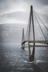 Obraz premium Scenic vertical photo on Sandnessjoen bridge very windy day, late autumn, low level clouds over Vefsnfjord. View from the left side. Car travel by nordic roads to Norway