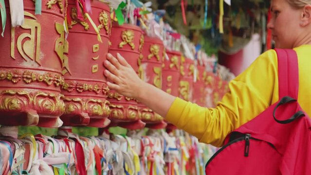 Person pilgrim woman touching turning spinning Buddhist prayer wheel at Buddhist monastery. Prayer wheels in Buddhist stupa temple. Buddhism religion concept