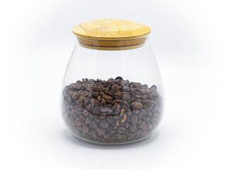 whole dark roast brown coffee beans in round glass jar or container with wooden top isolated on white background. front side view. number one most popular morning drink in the world to give energy