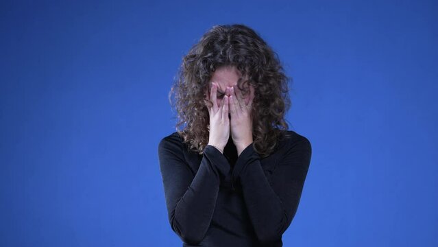 Frustrated Woman experiencing regret and confusion about past memories, female person in 20s covering face in shame and anxiety standing on blue background