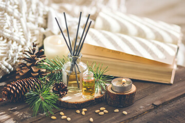 Assortment of natural Christmas essential oils in small bottles. Candles, branches of fir tree, home aroma diffuser. Aromatherapy, cozy atmosphere, holiday festive mood. Close up macro, wooden table