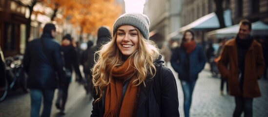 A happy woman is pictured in a black winter coat as she walks down a city street embodying the hipster lifestyle and enjoying her autumn vacation surrounded by people of different background