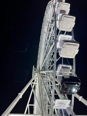 side shot of a white illuminated ferris wheel at night in a christmas amusement park