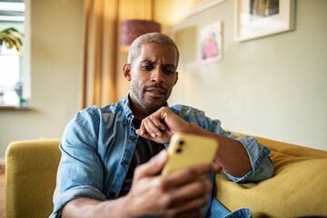 Serious middle aged man holding smartphone on sofa