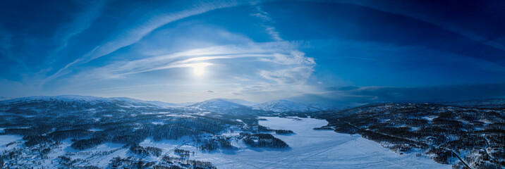 Very wide scenic aerial panorama on frozen lake, mountains with snow mobile traces, sunny blue sky with arched plane traces, contrails. Scandinavian white winter landscape, Norway, Sweden
