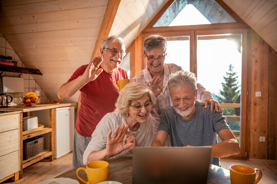 Senior friends having video call on laptop in wood cabin - Powered by Adobe
