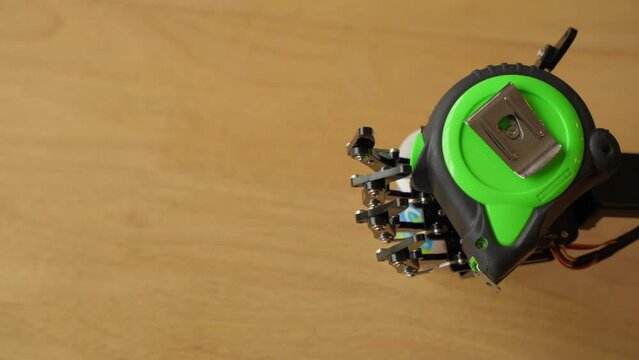 Robotic Hand Holding a Green Measuring Tape.