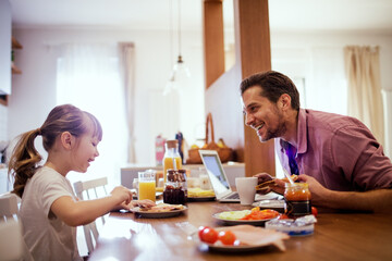 Happy little girl having breakfast with her father in the kitchen