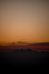 View of silhouettes of mountains and low colorful clouds at sunset.