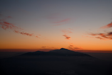 Colorful sunset over mountain peak silhouette surrounded by low weightless clouds