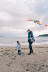 Smiling mom stands near a little girl with a kite in her hand on the seashore