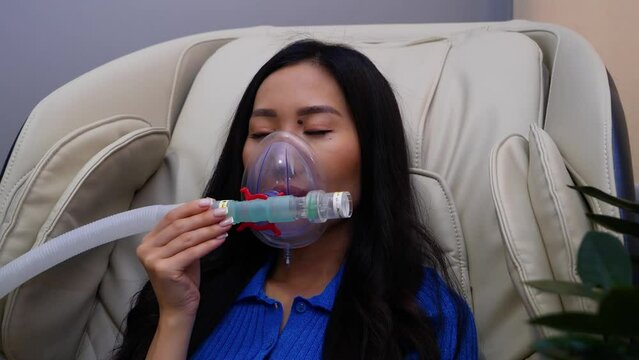 A girl sits on a massage chair and breathes in an oxygen mask
