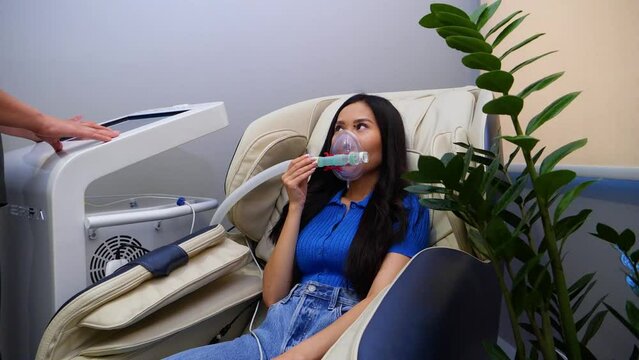 A girl sits on a massage chair and breathes in an oxygen mask