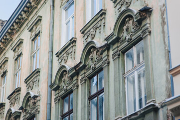 Fototapeta premium Windows with wooden frame. Neoclassical building with sandriks, porticoes and mascarons in the form of plant reliefs and head sculptures. Green and beige facade of an old house in Lviv, Ukraine.